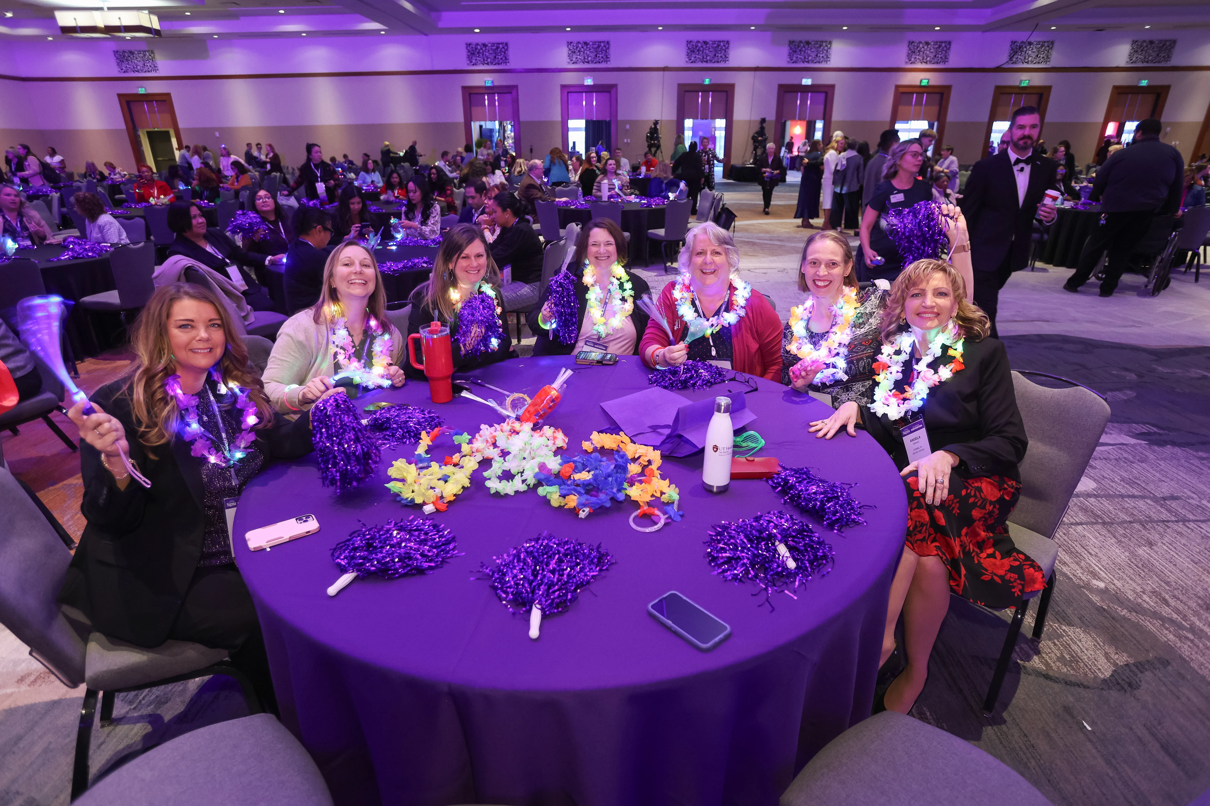 Group of women smiling and sitting at a table at event with event regalia.